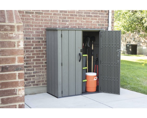 Gartenschrank mit geöffneter Tür neben einem Backsteingebäude, gefüllt mit Gartengeräten und einem Getränkebehälter.