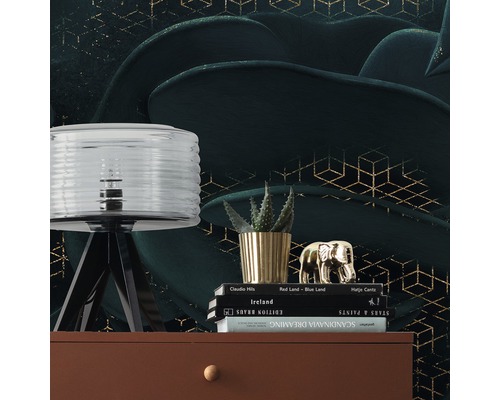 Dekorative Szene mit Lampe, Pflanze, Dekofigur und Büchern auf einer Kommode vor einer gemusterten Tapete