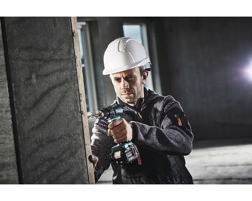 Mann mit Schutzhelm bohrt mit einer Akku-Bohrmaschine in ein Werkstück