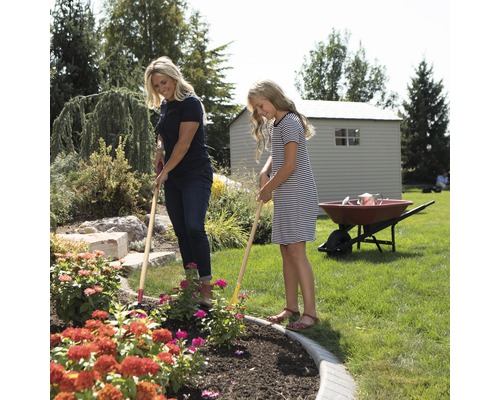 Eine Frau und ein Mädchen jäten ein Blumenbeet im Garten mit Gartenharken.