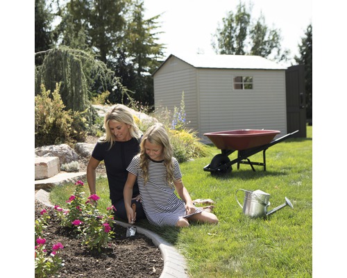 Gartenszene mit Gartenhaus, Schubkarre, Gießkanne und zwei Personen beim Pflanzen von Blumen
