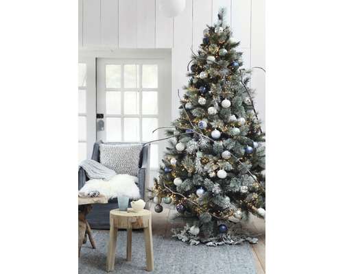 Dekorierter Weihnachtsbaum mit Lichtern, Christbaumkugeln und rustikalen Dekorationen in einem Wohnzimmer.