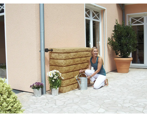 Szene mit einer Frau, die neben einem Regenwassertank kniet, mit Blumen in Töpfen und einer Gießkanne in einem Garten.