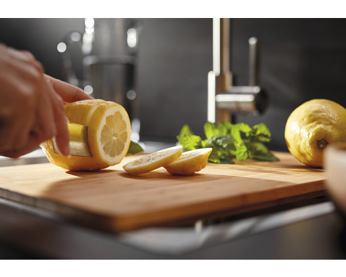 Eine Person schneidet eine Zitrone mit einem Küchenmesser auf einem Schneidebrett. Minze liegt daneben.