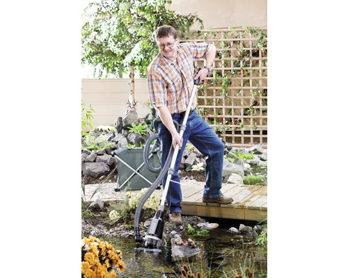 Mann reinigt Teich mit Teichsauger in Gartenszene.