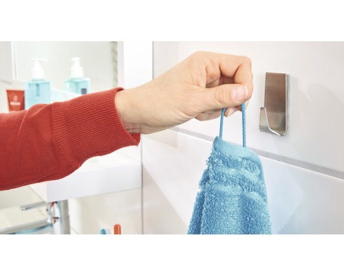 Eine Hand hängt ein blaues Handtuch an einen Handtuchhaken im Badezimmer