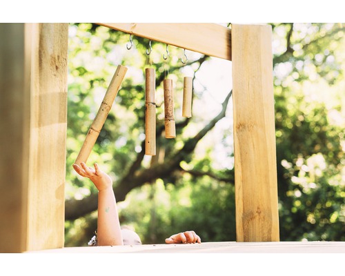Szene mit einem Kind, das ein Windspiel aus Bambus berührt, das an einem Holzrahmen hängt.