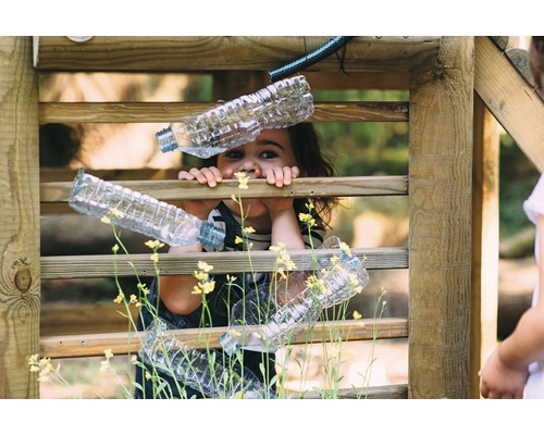 Mädchen spielt mit Plastikflaschen in einem Holzzaun