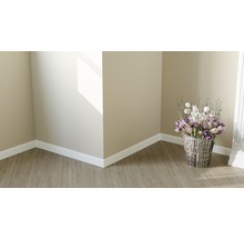 Helle Ecke eines Raumes mit Laminatboden, Sockelleisten und einem Blumenarrangement in einem silberfarbenen Korb