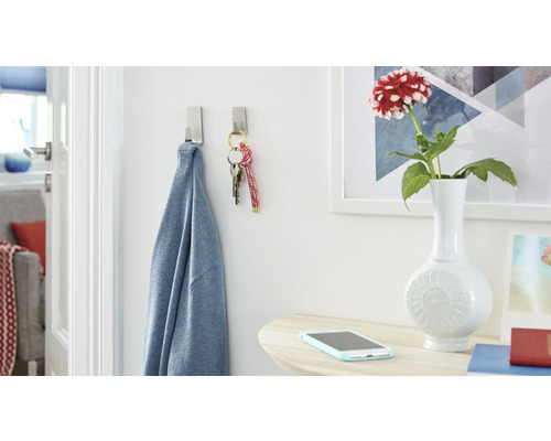 Szene mit zwei Klebehaken, an denen ein Hemd und ein Schlüsselbund hängen, sowie einem Tisch mit Blumenvase und Smartphone