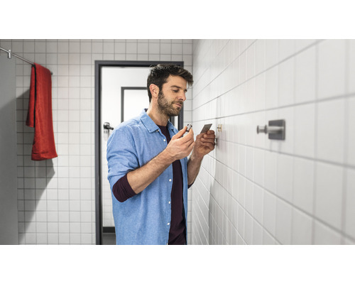 Mann befestigt einen Haken an einer gefliesten Badezimmerwand