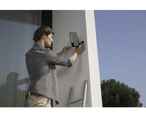 Ein Mann montiert eine Außenlampe an einer Fassade.