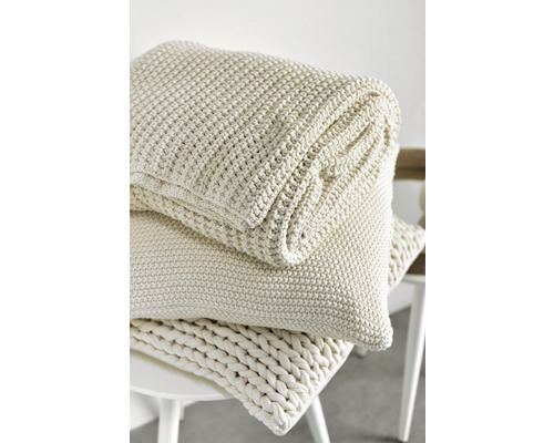 Gestapelte, gestrickte Tagesdecke und Kissen auf einem Hocker