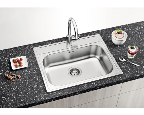 Spüle aus Edelstahl mit Armatur auf einer Küchentheke mit Speisen.