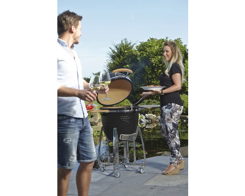Szene im Freien mit einem Keramikgrill, zwei Personen und Gartendekoration.
