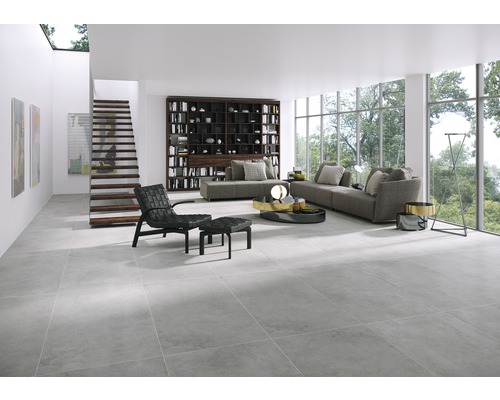 Helles Wohnzimmer mit grauen Bodenfliesen, Sofa, Bücherregal und Treppe