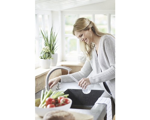 Frau am Waschbecken in einer hellen Küche mit Armatur und frischem Gemüse