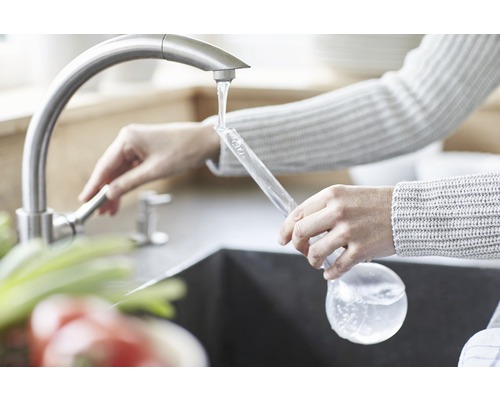 Frau befüllt Messkolben am Wasserhahn in der Küche