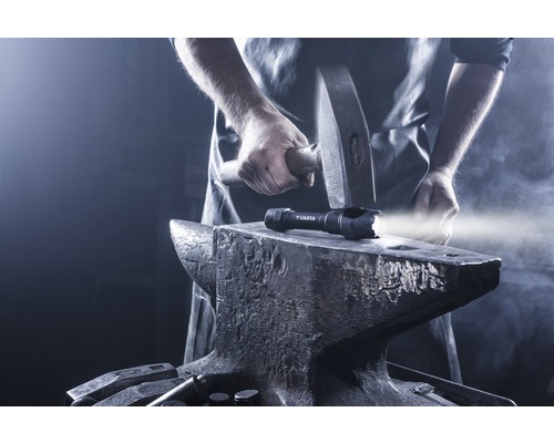 Eine Varta Taschenlampe auf einem Amboss, mit einem Hammer darüber