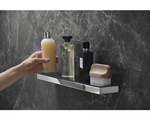 Wandregal im Badezimmer mit Pflegeprodukten und Hand, montiert an einer grauen Marmorwand.