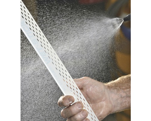 Ein Mann reinigt ein Putzprofil mit Löchern mit einem Wasserstrahl.