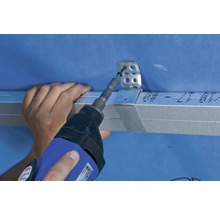 Handwerker befestigt eine Metallschiene mit einem Schraubendreher an einer Wand.