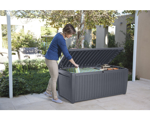 Frau öffnet eine wetterfeste Aufbewahrungsbox im Garten für Kissen und Gartengeräte