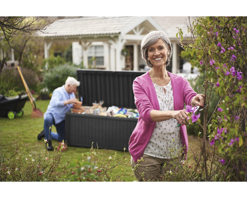 Frau schneidet Büsche im Garten mit einer Gartentruhe im Hintergrund