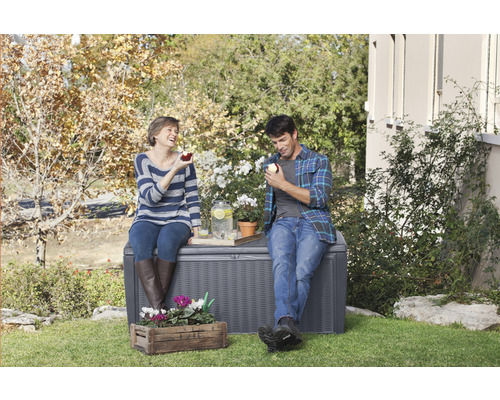 Szene mit einer Aufbewahrungsbox im Garten, auf der ein Paar sitzt und Getränke genießt