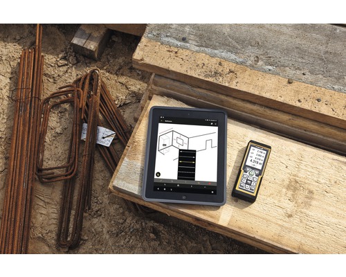 Tablet mit Bauplan-App und Laser-Entfernungsmesser auf Holz neben Bewehrungsstahl