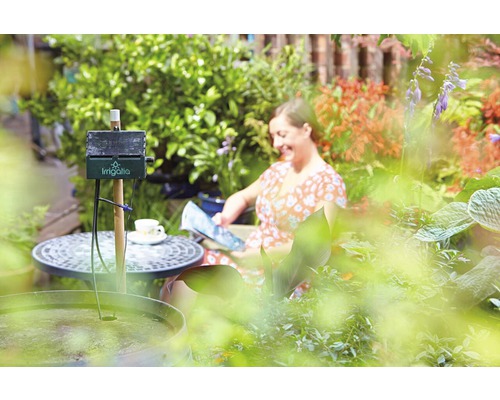 Automatische Bewässerung im Garten mit lesender Frau im Hintergrund