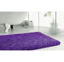 Lila Badteppich vor einer Badewanne in einem hellen Badezimmer.
