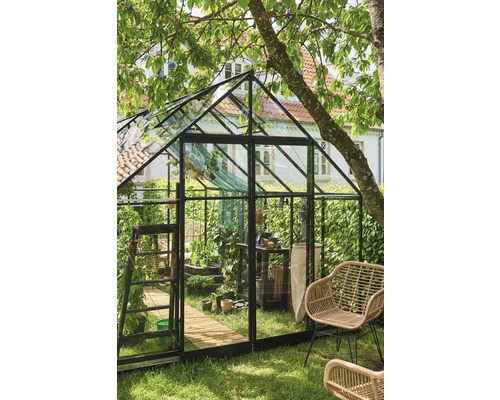 Gewächshaus mit Pflanzen und Gartengeräten in einem Garten