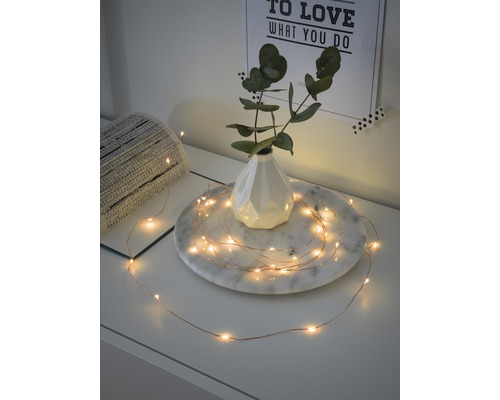 Dekorative Lichterkette mit feinen LEDs und Kupferdraht, arrangiert um eine Vase auf einem Tisch