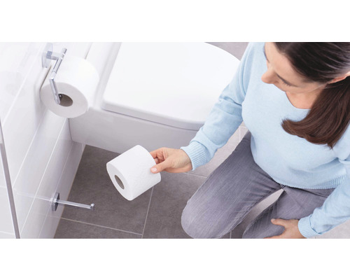 Frau entnimmt Toilettenpapier aus einem Spender im Badezimmer.