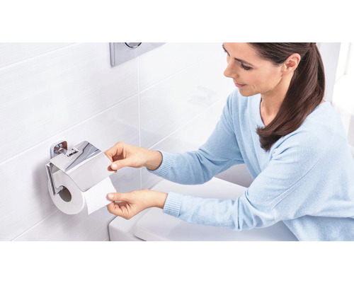 Frau entnimmt Toilettenpapier aus einem verchromten Toilettenpapierhalter mit Deckel.