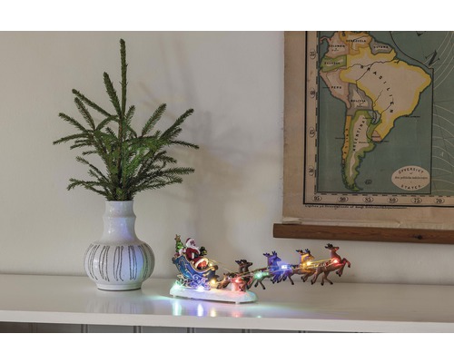Dekorative Szene mit Tannenzweigen in einer Vase, einer beleuchteten Weihnachtsmannschlittenfigur und einer Karte von Südamerika.