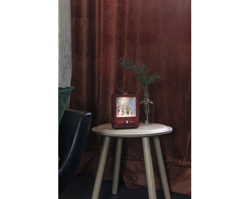 Dekorative Schneekugel in Fernsehoptik auf kleinem Tisch mit Dekoration