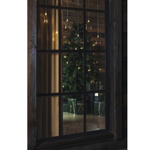 Blick durch ein Fenster auf einen Weihnachtsbaum mit Geschenken und Sternenlichterkette