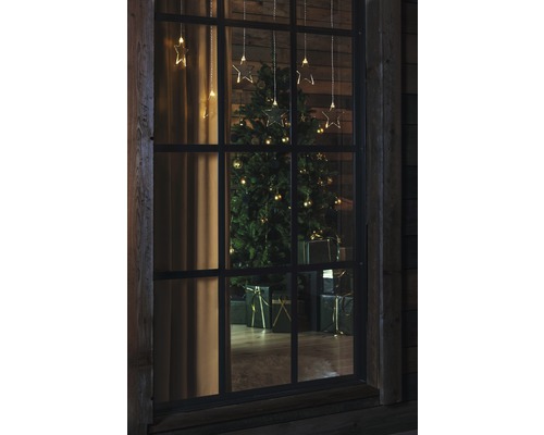 Blick durch ein Fenster auf einen Weihnachtsbaum mit Geschenken und Sternenlichterkette
