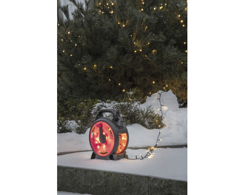 Lichterkette auf Kabeltrommel im Schnee vor beleuchtetem Baum