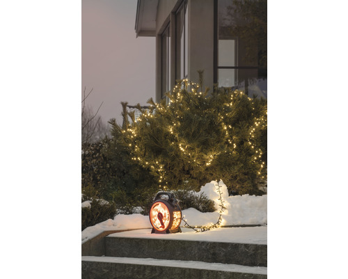 Winterliche Gartenszene mit beleuchtetem Busch und dekorativer Laterne auf einer Treppe