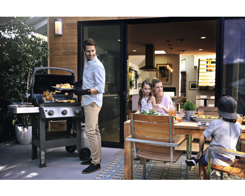 Familie grillt im Freien mit einem Gasgrill und Holzesstisch.