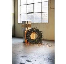 Dekorative Weihnachtsszene mit Geschenkstapel, Tannenkranz und Lichterkette vor einem Fenster