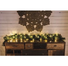 Dekoratives Sideboard mit Tannengirlande und Lichterkette sowie einem Wandteppich an der Wand.
