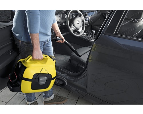 Mann saugt mit einem gelben Mehrzwecksauger den Innenraum eines Autos.