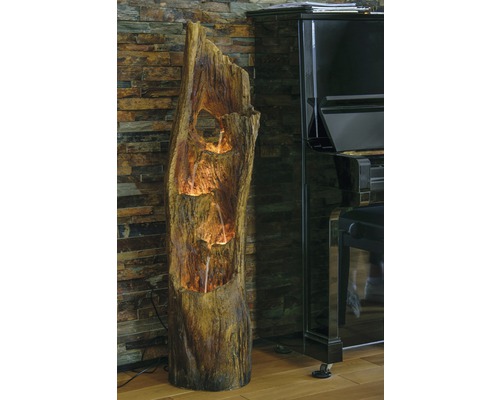 Dekorativer Zimmerbrunnen in Baumstammoptik neben einem Klavier