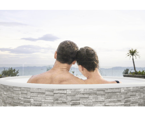 Ein Paar entspannt in einem Outdoor Whirlpool mit Steinverkleidung und Blick auf das Meer.
