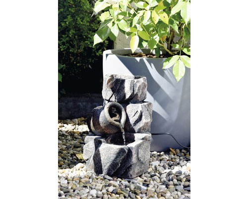 Dekorativer Gartenbrunnen mit Steinoptik und Wasserkrug auf Kies