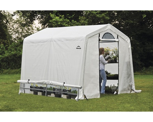 Gewächshaus mit Regalen und einer Frau, die Pflanzen gießt